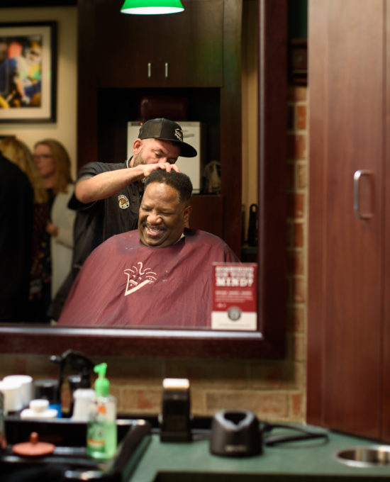 barber giving haircut while patron laughs