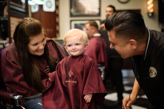 Barber and mother of child smiling at child during first haircut