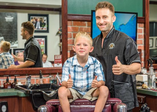 Barber and child giving two thumbs up after a haircut